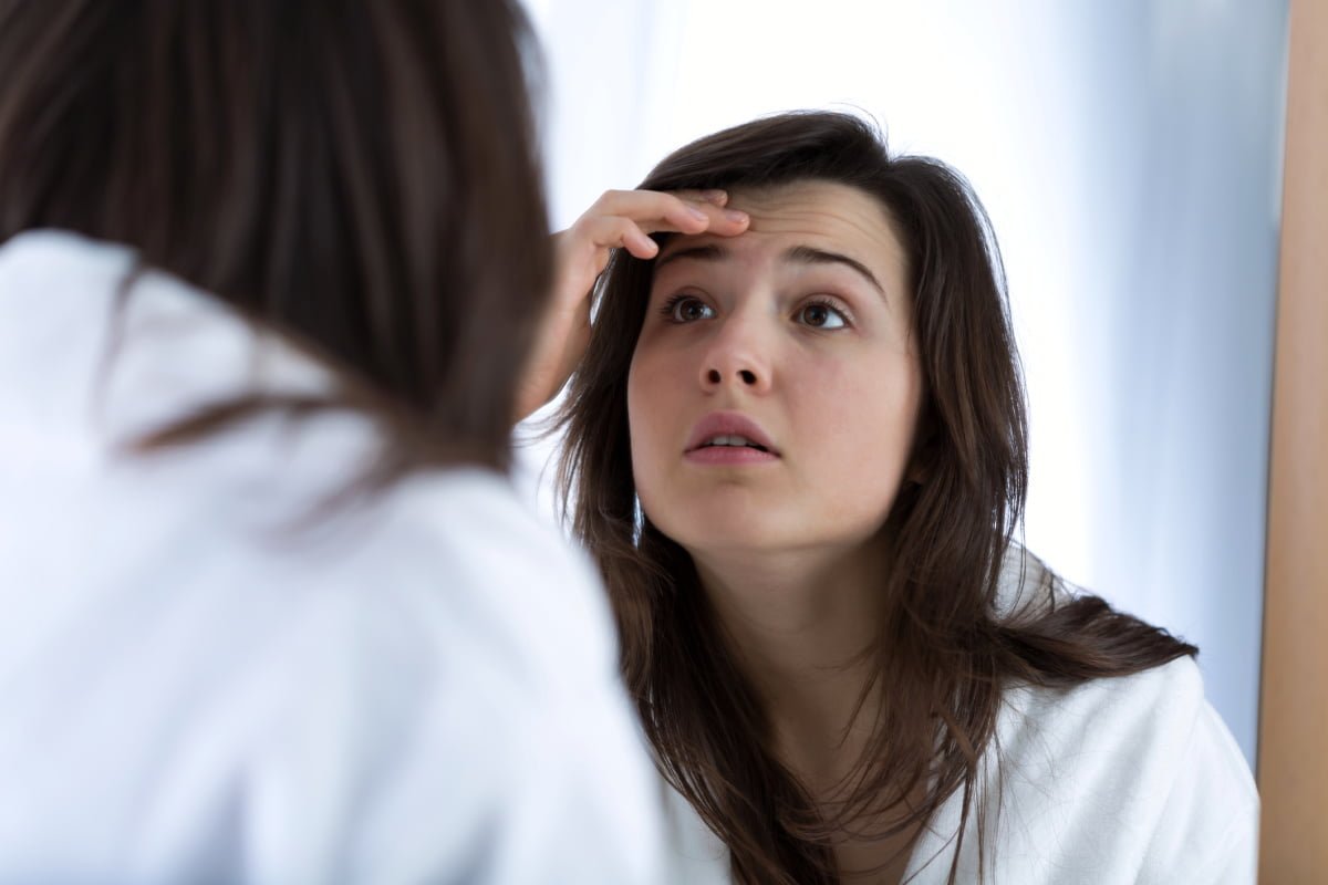 Woman Looking at Forehead Wrinkles in Mirror Before BOTOX Treatment