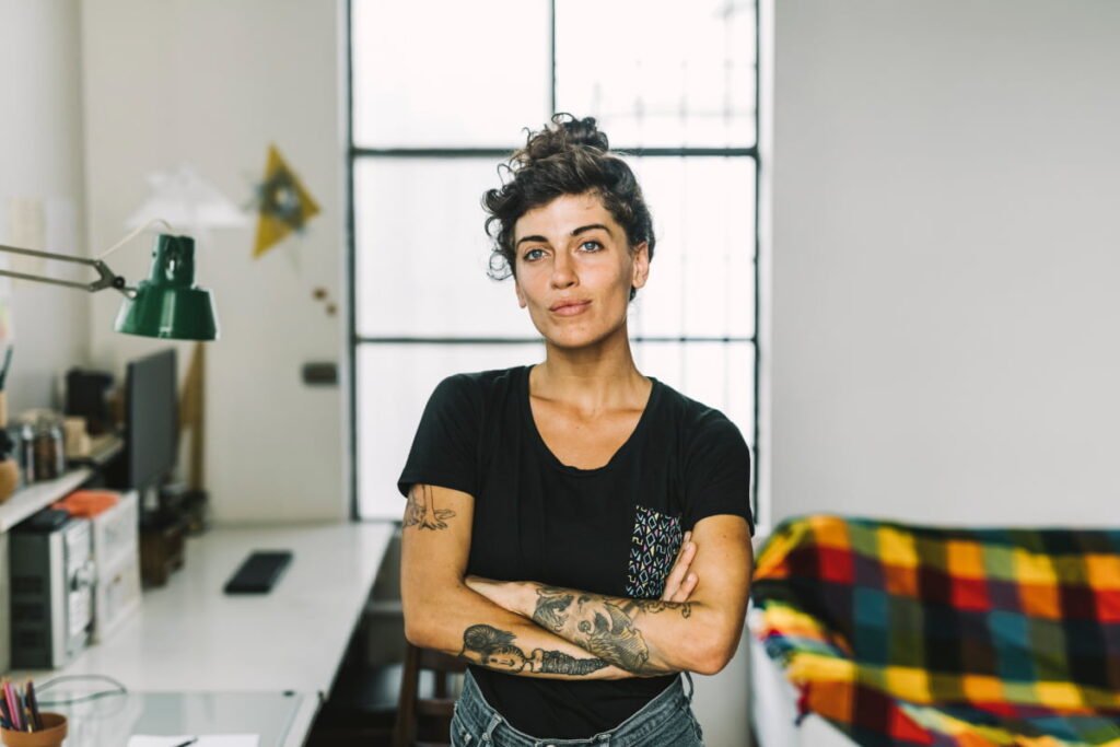 Woman with tattoos smiles with arms over chest