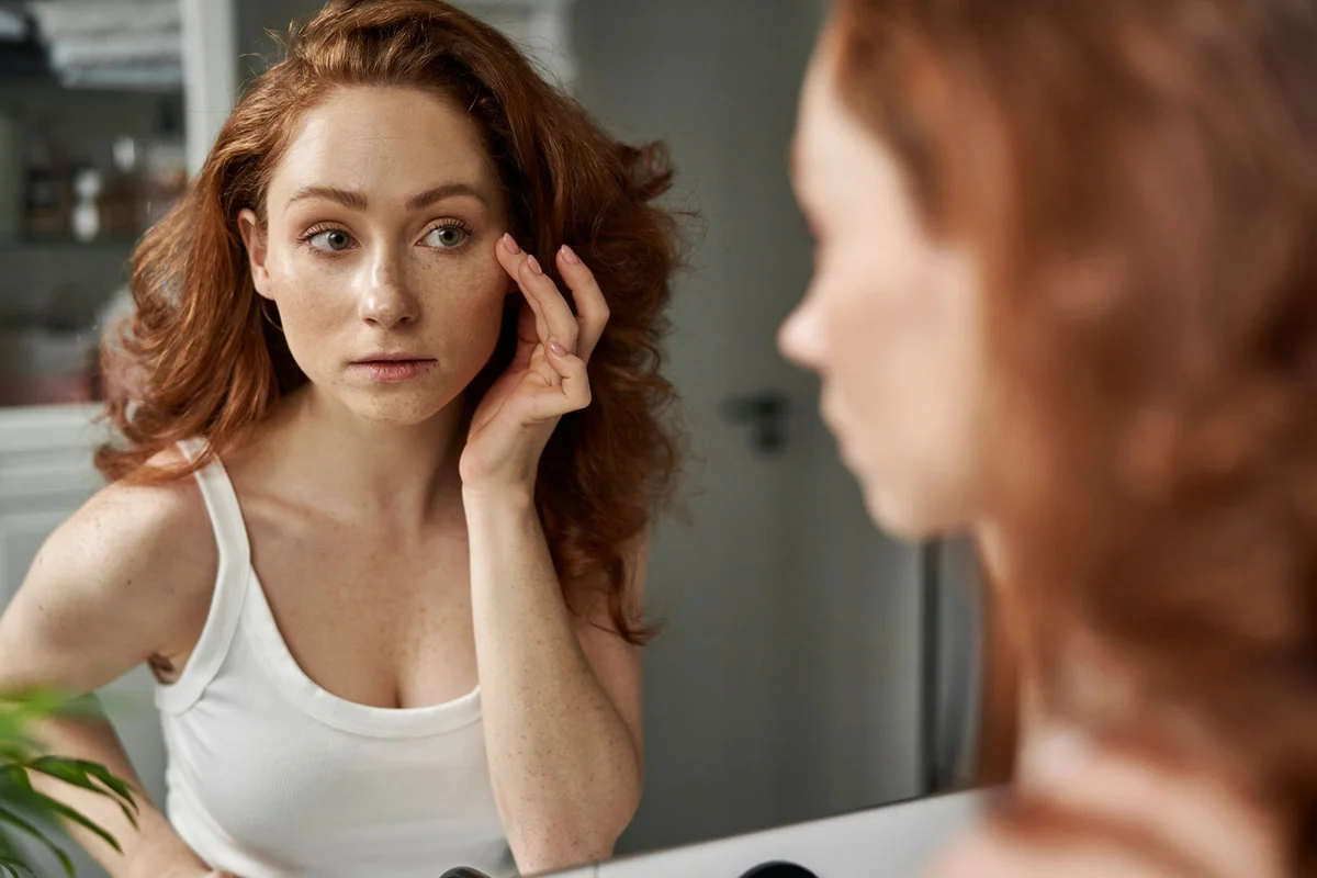 Asheville woman looking at cheekbones in mirror after getting facial fillers
