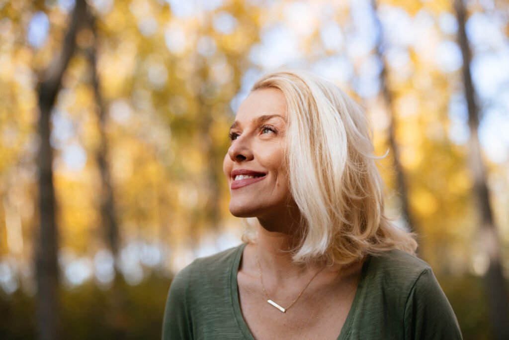 Smiling woman enjoying sunlight on her face while standing in the woods