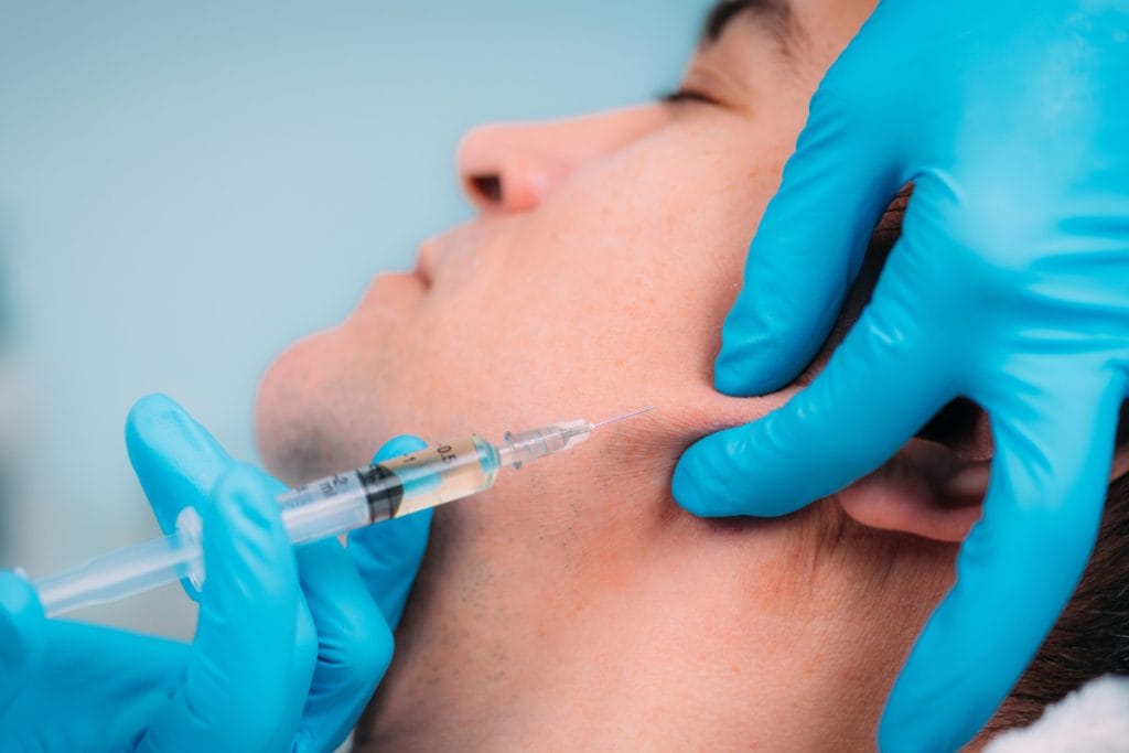 Close up of man getting filler injections to enhance jawline contour